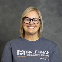 Smiling person wearing glasses and a McLennan Community College T-shirt in a studio-style portrait.