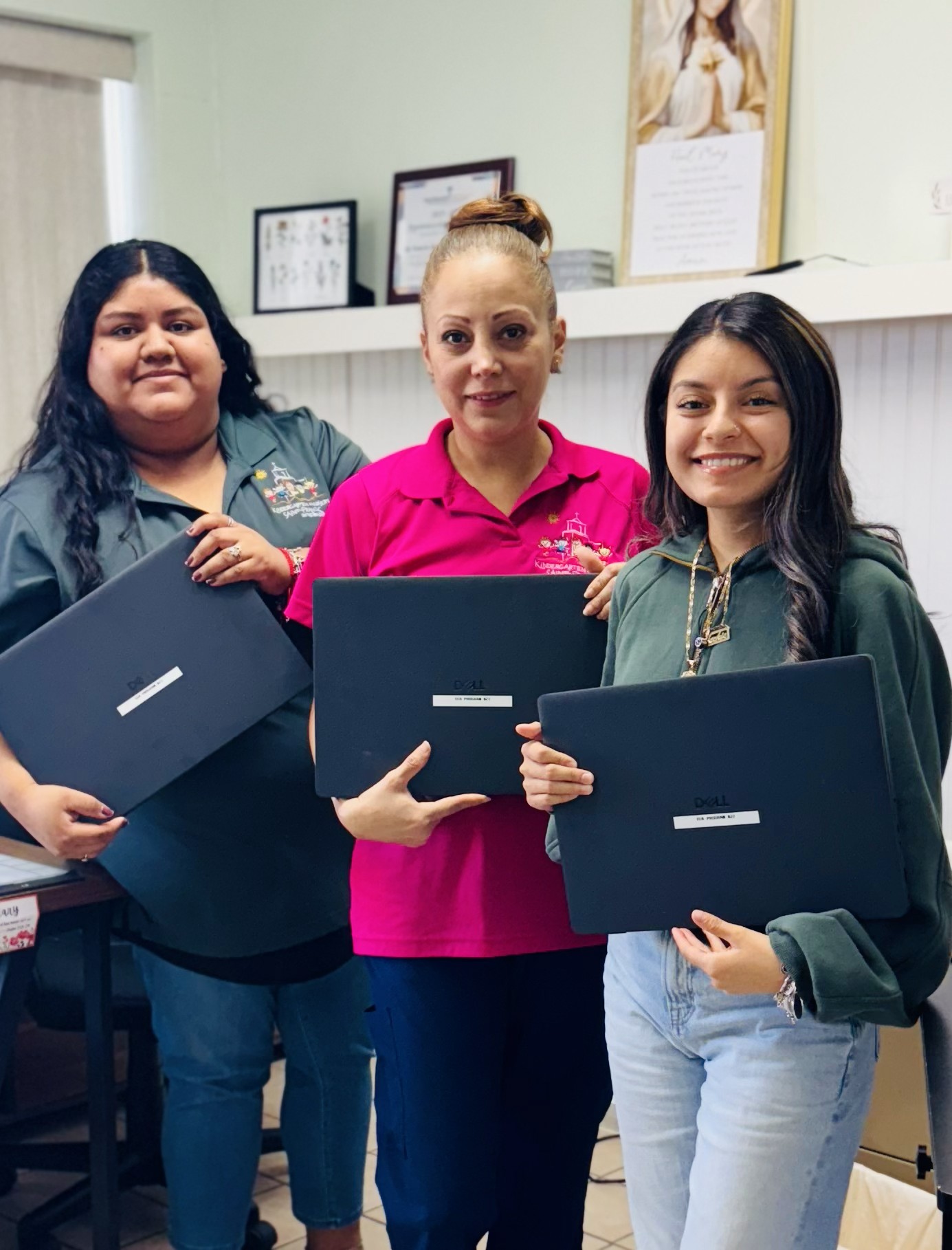 Three women holding laptops, smiling together in an office setting. The image conveys a sense of teamwork and technology use.