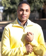 Starlen standing outside wearing a yellow sweater and holding the cuff of his sleeve