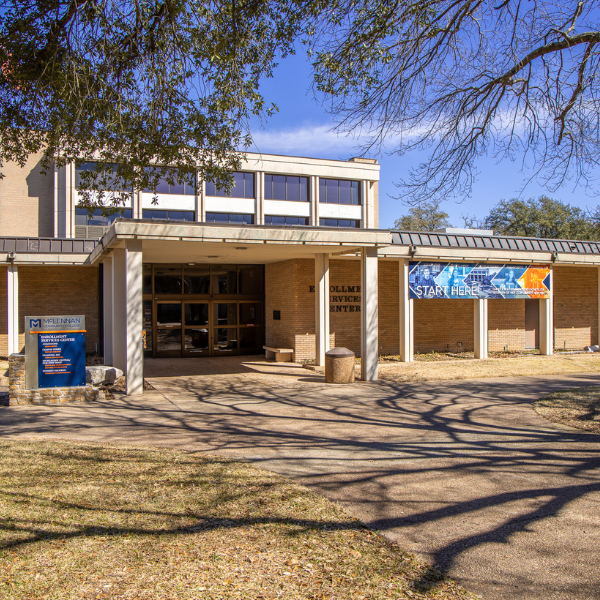 Front entrance of the McLennan Community College Highlander Central student services building on a sunny day, featuring a covered walkway, campus signage, and a “Start Here” banner along the front exterior.