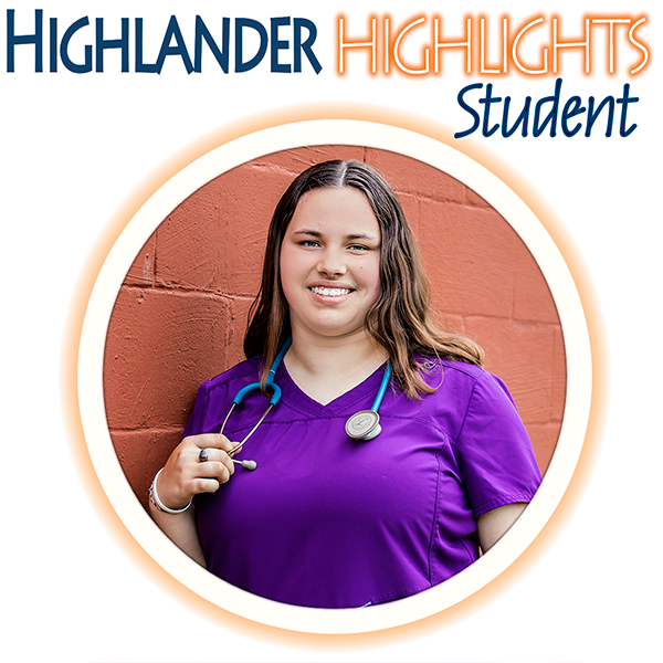 Student featured in Highlander Highlights, wearing purple scrubs and holding a stethoscope, standing in front of an orange brick wall.