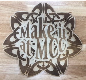 Wooden sign with the text "Make it at MCC" designed in an ornate floral pattern.