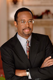 Portrait of Ben Carson in a suit with arms crossed, smiling confidently.